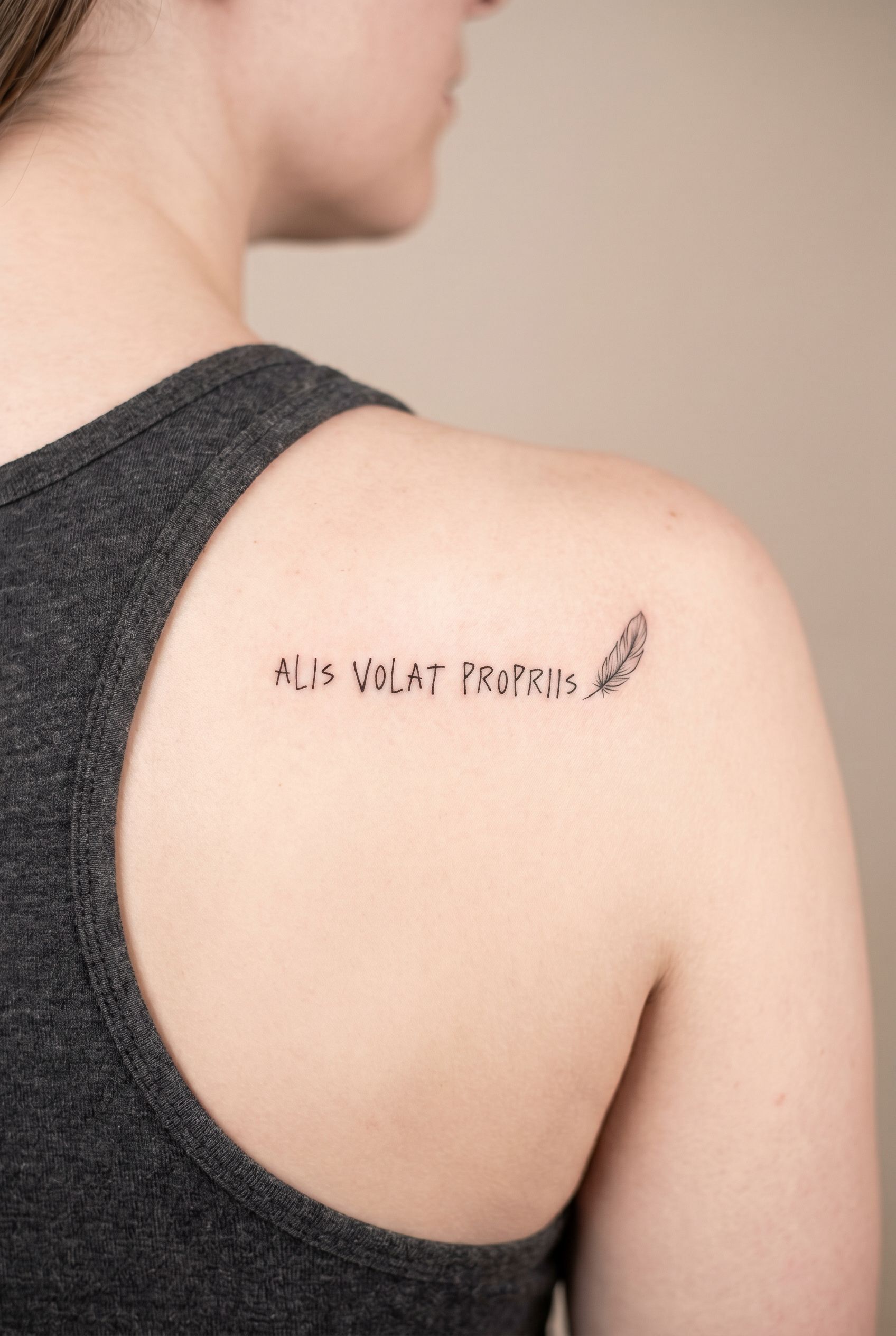 Tatouage de la phrase latine Alis volat propriis sur l'omoplate