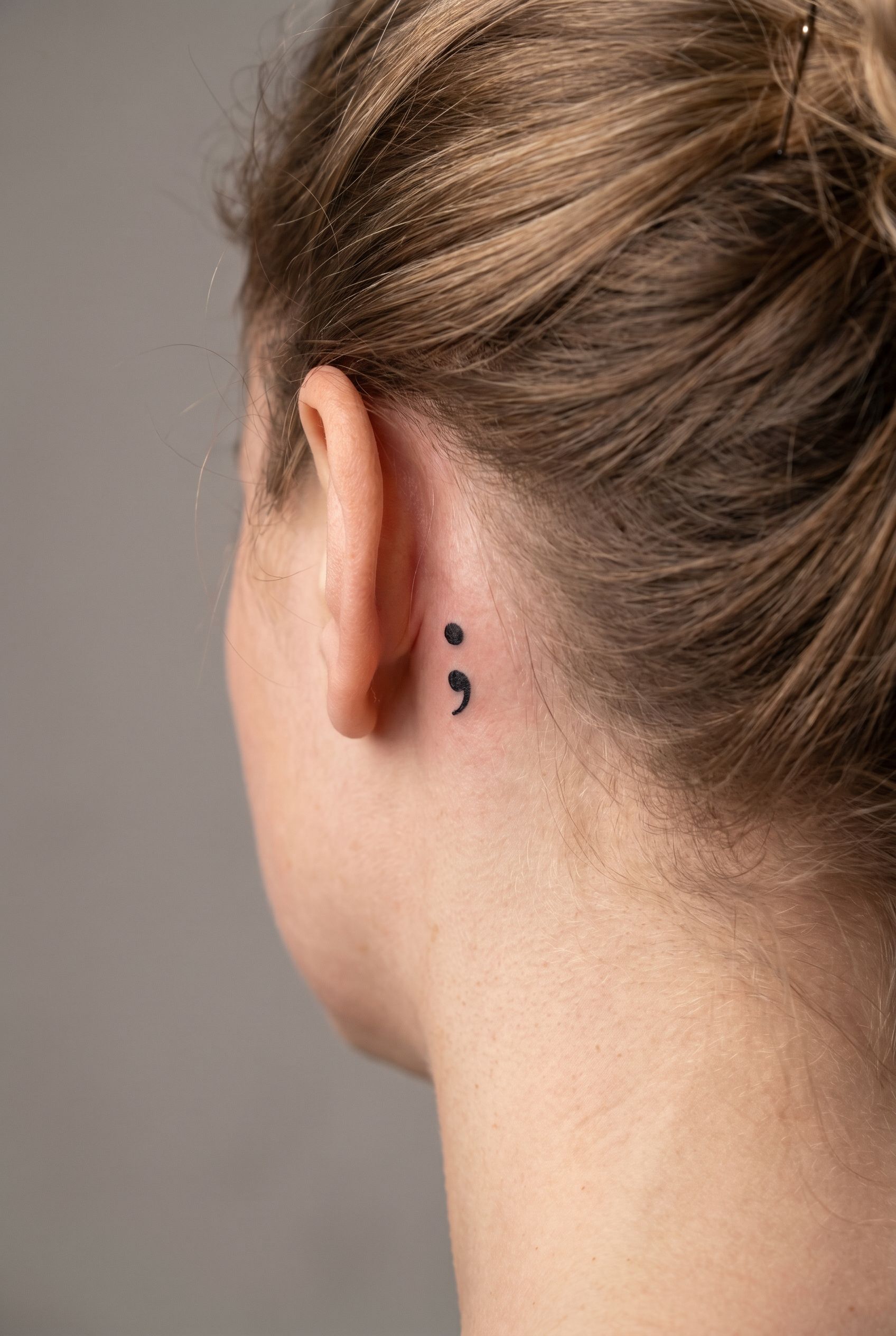 Petit tatouage point-virgule derrière l'oreille d'une femme